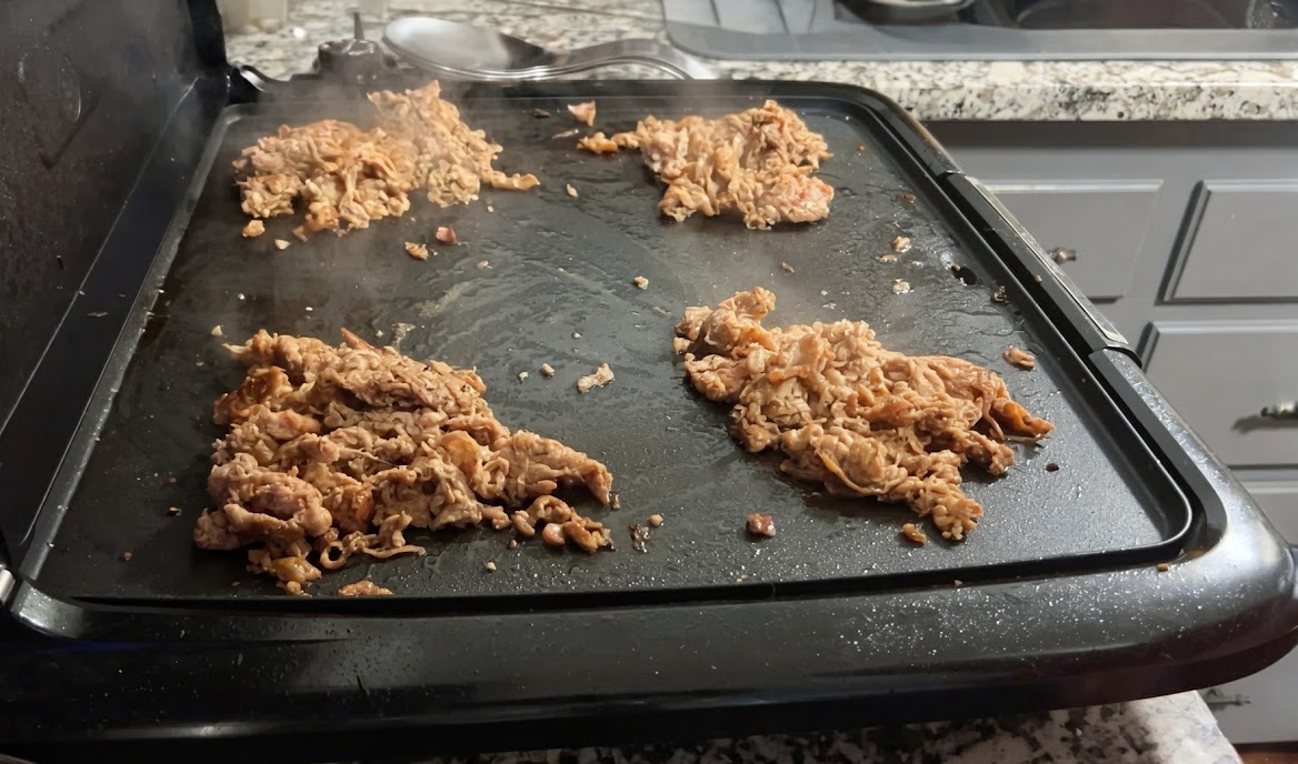 Steak divided into four piles on the griddle
